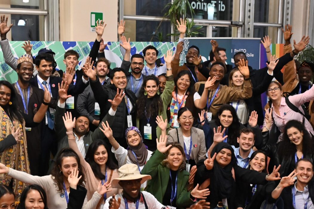 A diverse group of young climate leaders smiling and raising their hands together at Youth4Climate Call for Solutions event.
