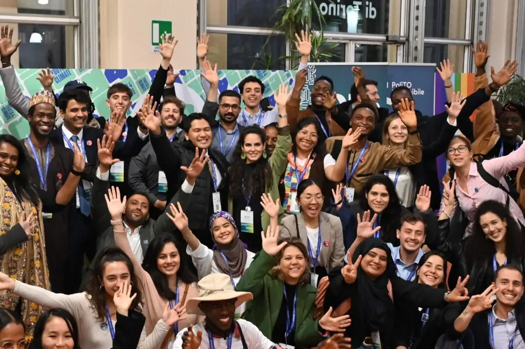 A diverse group of young climate leaders smiling and raising their hands together at Youth4Climate Call for Solutions event.