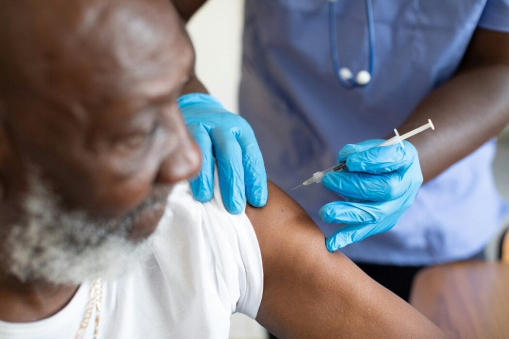 COVID-19 vaccination being administered to an elderly man by a healthcare professional wearing blue gloves, showcasing health and immunisation services provided by SMEPEAKS.