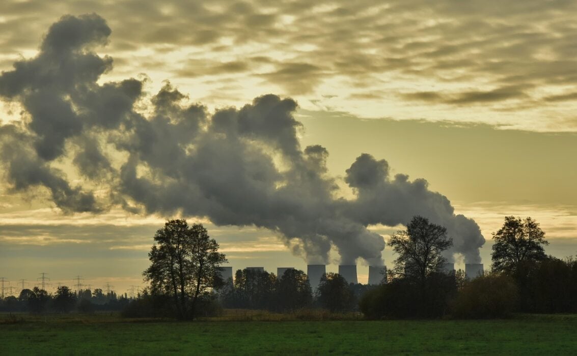 Industrial pollution with cooling towers releasing smoke over a green landscape at sunset, illustrating environmental impact of energy production.