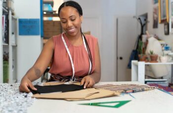 Ihifix AfriScale Business Fund 2025 - Efficient female fashion designer working on garment patterns in a creative atelier. SMEPEAKS branding in the background showcases expertise in fashion design and bespoke tailoring services.